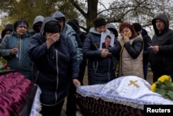Relatives mourn at the coffins of Iryna Kharbaka and Oleksandr Khodak, who were among 59 civilians killed in a Russian missile attack, amid Moscow's ongoing invasion of Ukraine, at their funeral in the village of Hroza, near Kharkiv, Ukraine, Oct. 9, 2023.