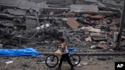 A Palestinian child walks with a bicycle by the rubble of a building after it was hit by an Israeli airstrike, in Gaza City, Oct. 8, 2023.