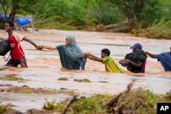 FILE - Residents cross a road damaged during flooding in Tula, Tana River county in Kenya on Nov. 25, 2023.