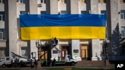 Municipal workers in the city of Kherson, Ukraine, decorate the wall of the regional administration building with a national flag to mark one year since Ukrainian troops retook the city from the Russian army, Nov. 10, 2023.