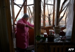 A woman sweeps broken windows glass in her flat after the explosion of a downed Russian drone in a yard among residential buildings in Kyiv, Ukraine, on Nov. 25, 2023.
