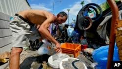 FILE - Kevin Hendershot pours ice into a bucket outside his tent in 'The Zone' homeless encampment, July 14, 2023, in downtown Phoenix.