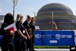 People walk near a logo for the COP28 U.N. Climate Summit, in Dubai, United Arab Emirates, Nov. 29, 2023.