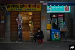 FILE - A vendor sits outside his store selling souvenirs in Xiamen in southeast China's Fujian province on Dec. 27, 2023.