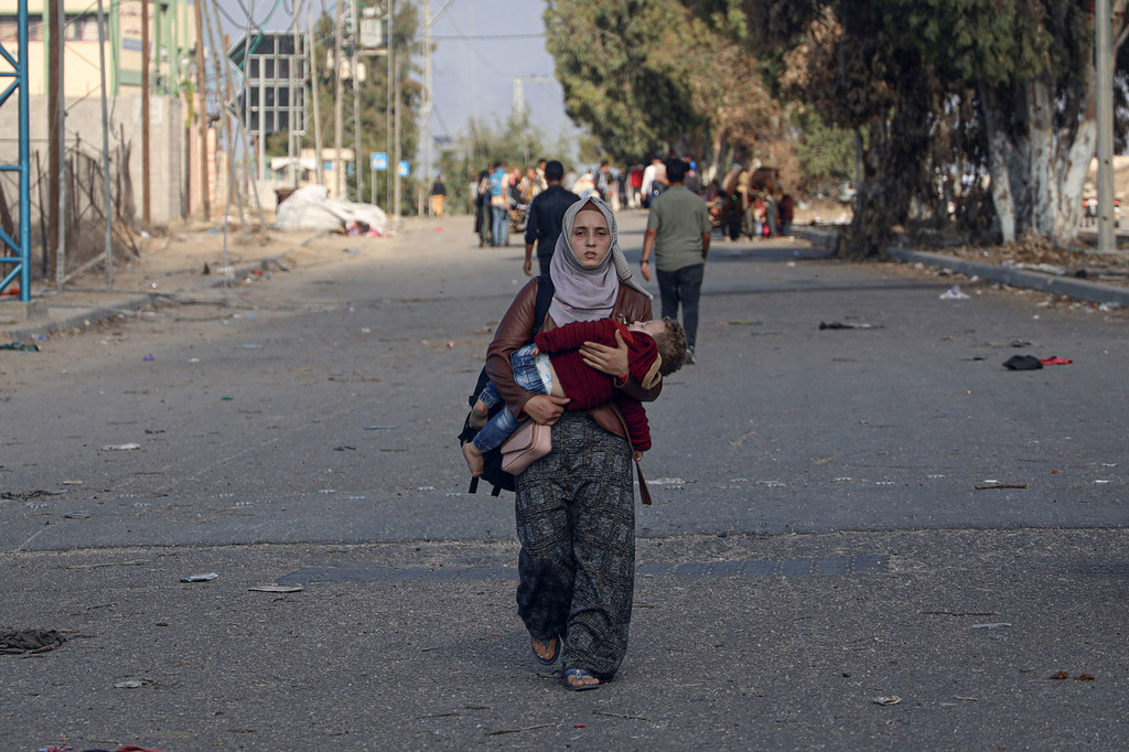 A woman carries a child while heading toward southern Gaza.