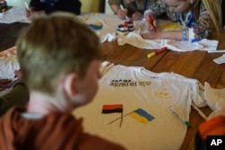 FILE - A boy decorates a T-shirt with the words "Glory to Ukraine" at a recovery camp for children and their mothers affected by the war, near Lviv, Ukraine, on May 3, 2023.