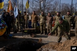 A Ukrainian serviceman throws soil into the grave of Yehor Voloshyn, 27, a Ukrainian serviceman, in Pavlohrad, Dnipropetrovsk region, Ukraine, Feb. 26, 2024. The sergeant from the 3rd Assault Brigade was killed in the fighting near Avdiivka on Feb. 21, 2024