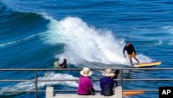 FILE - Visitors to the pier watch surfers ride the waves in Huntington Beach, Calif., on Sept. 19, 2023.