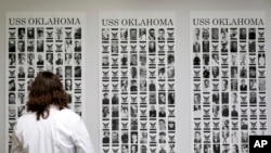 Defense POW/MIA Accounting Agency forensic anthropologist Carrie Brown looks at photos of service members from the USS Oklahoma on a wall at Offutt Air Force Base, May 20, 2024, in Bellevue, Neb.