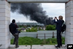 Foreign journalists report from an observation point while smoke rises after a Russian attack in Kharkiv, Ukraine, May 17, 2024.