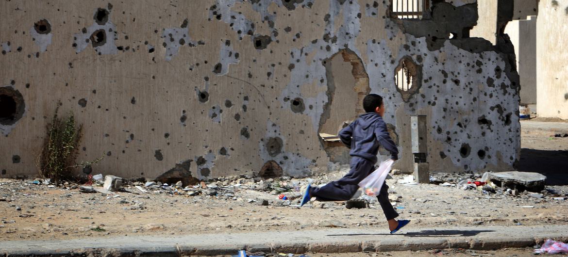 A boy runs past damaged buildings, defaced by shelling during the conflict, on his way home from shopping, in the city of Sirte. (file)