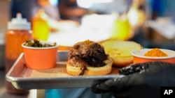 A line cook carries a pulled pork sandwich at a barbecue restaurant in Cincinnati, Ohio, June 12, 2024.