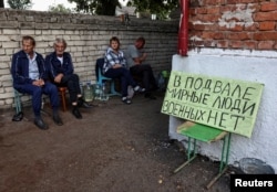 Residents sit near a shelter where they hid during fighting between Ukrainian and Russian forces in Sudzha, Russia, which is controlled by the Ukrainian army, on Aug. 16, 2024. The sign reads: "There are peaceful people in the basement, there are no soldiers."