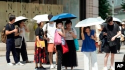 FILE - Pedestrians holding parasols stand under an intense sun at Ginza shopping street in Tokyo, July 8, 2024.