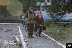 An elderly woman is assisted by emergency services personnel after a Russian strike that hit a home for the elderly in Sumy, Ukraine, Sept. 19, 2024. (Ukraine's Emergency Service via AP)