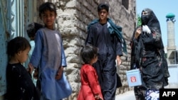 FILE - An Afghan health worker, right, walks towards children standing in front of their home during a polio vaccination campaign in the old quarters of Herat, Afghanistan, June 3, 2024.