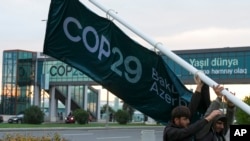 People adjust a banner outside the venue for the COP29 U.N. Climate Summit, Nov. 18, 2024, in Baku, Azerbaijan.