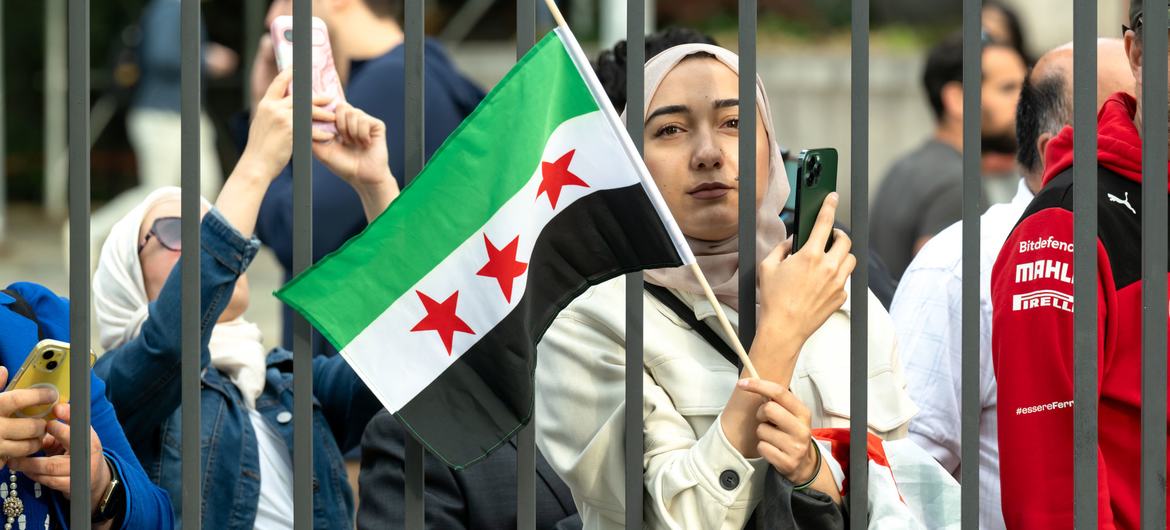 A woman holds the new Syrian flag outside UN Headquarters in New York. A woman holds the new Syrian flag outside UN Headquarters in New York.